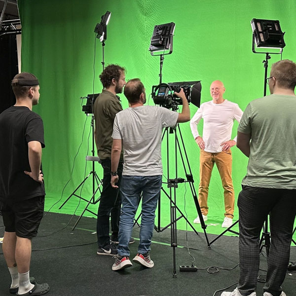 man in white standing in front of green screen with a camer in front of him