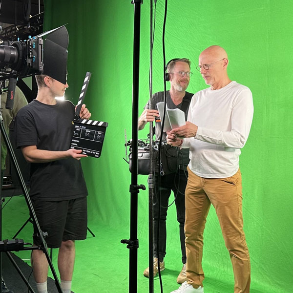 man in white standing in front of green screen with a camer in front of him